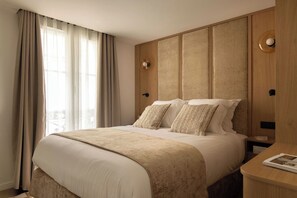Habitación de hotel con una cama grande, dos almohadas, una mesita de noche con lámpara y una ventana con cortinas.