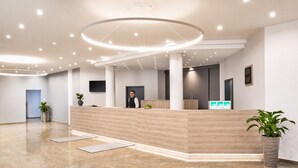 A modern reception area with a wooden reception desk, a large circular light fixture, and a potted plant.