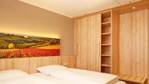 A bedroom with two beds, a wooden wardrobe, and a large landscape painting on the wall.