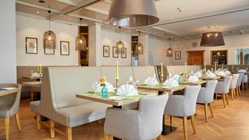 A restaurant with multiple tables set for dining, featuring a modern interior with pendant lighting and framed artwork on the walls.