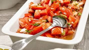 Un plat rectangulaire blanc contenant une salade de tomates, une cuillère et un petit bol d’olives.