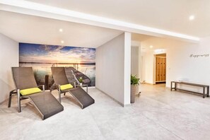 Una habitación moderna con un mural de atardecer, dos sillones de descanso, un banco y una pared con la palabra 'Happiness'.
