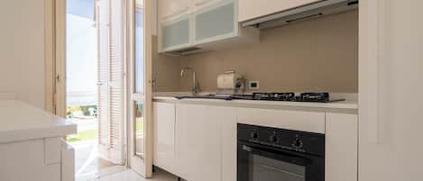 Una cocina moderna con armarios blancos, horno empotrado y una encimera con cafetera.