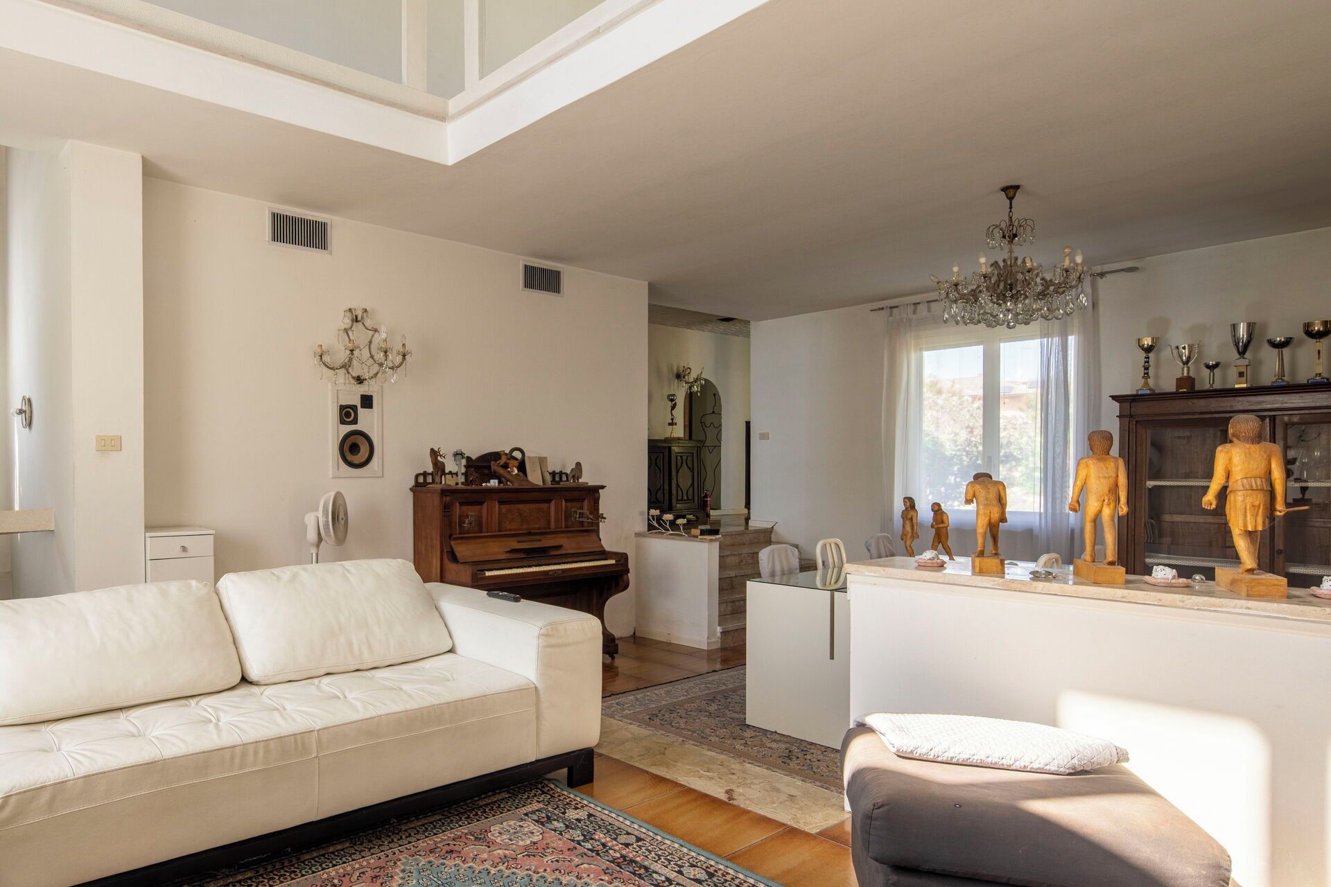 A living room with a white sofa, a piano, a chandelier, and a collection of statues.