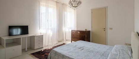 Un dormitorio con cama, televisor sobre un mueble bajo, cómoda, puerta y candelabro.