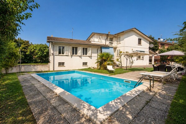 A two-story house with a swimming pool, outdoor furniture, and a garden.