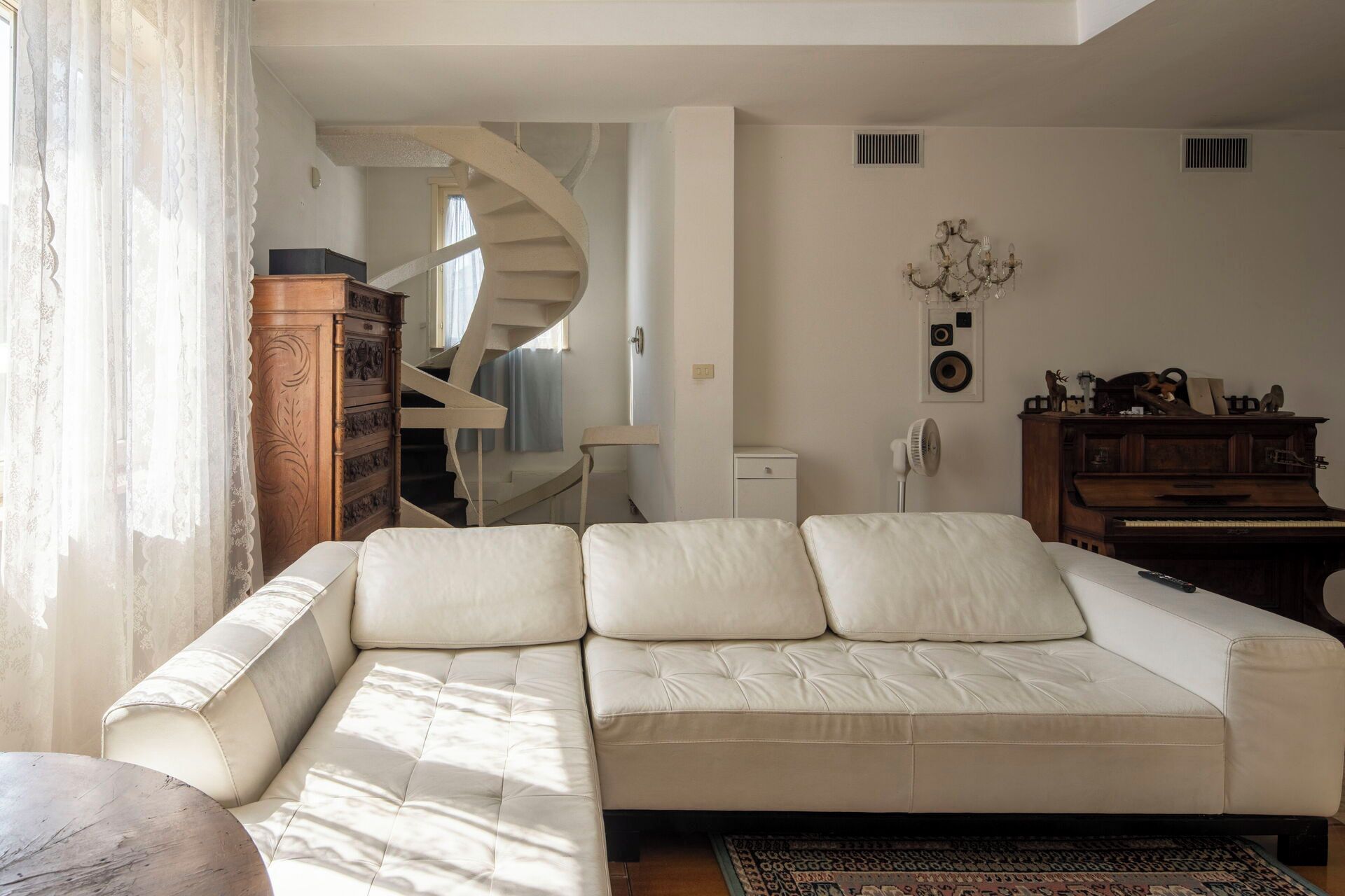 Una sala de estar con un sofá, un armario de madera, un piano y una escalera en espiral.