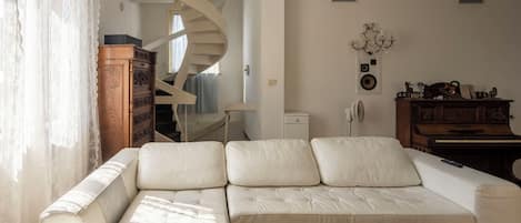 Un salon comprenant un canapé, un meuble en bois, un piano et un escalier en colimaçon.