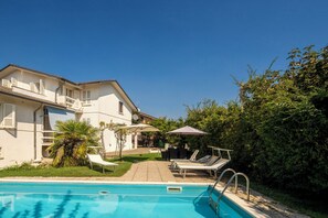 Ein Swimmingpool mit Liegestühlen und Sonnenschirmen, umgeben von einem Gebäude mit einem Balkon.