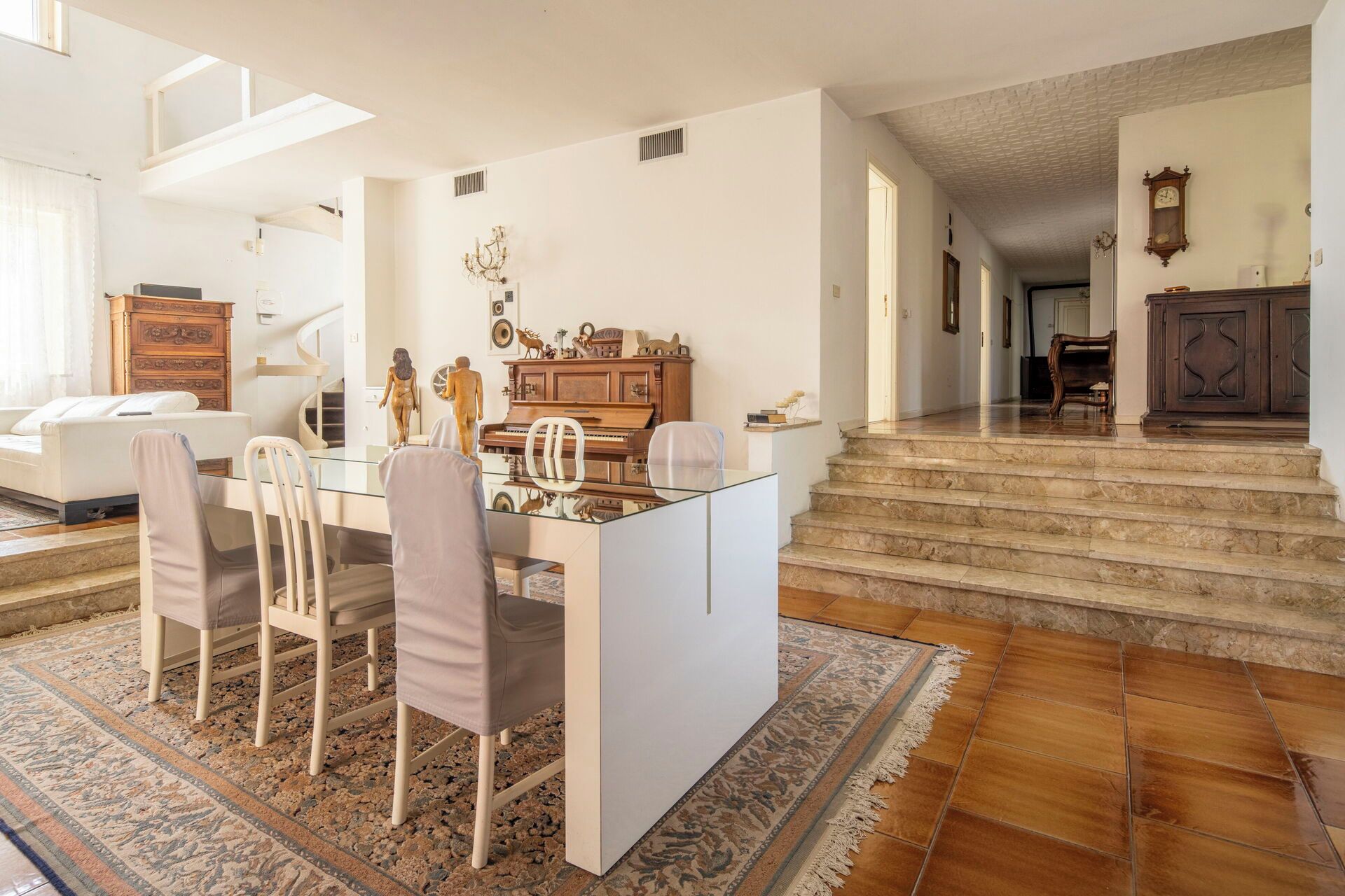 Un vaste espace de vie comprenant un coin repas avec une table en verre entourée de chaises, un piano et des objets décoratifs.