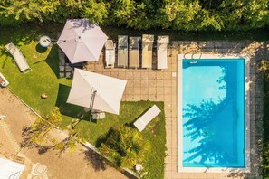 Une piscine bordée de chaises longues et de parasols, entourée d’une pelouse bien entretenue et d’arbres.