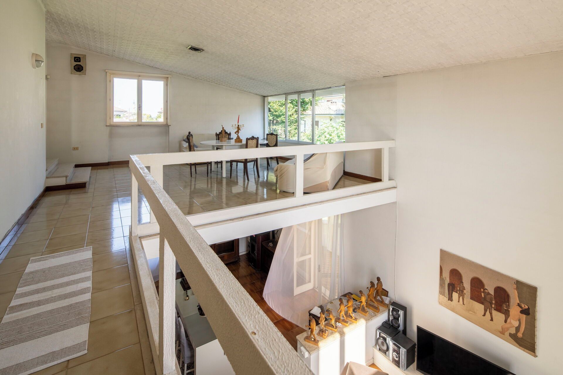 Una habitación amplia con techo alto, un balcón y un comedor con mesa y sillas.