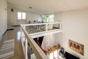 A spacious room with a high ceiling, a balcony, and a dining area with a table and chairs.