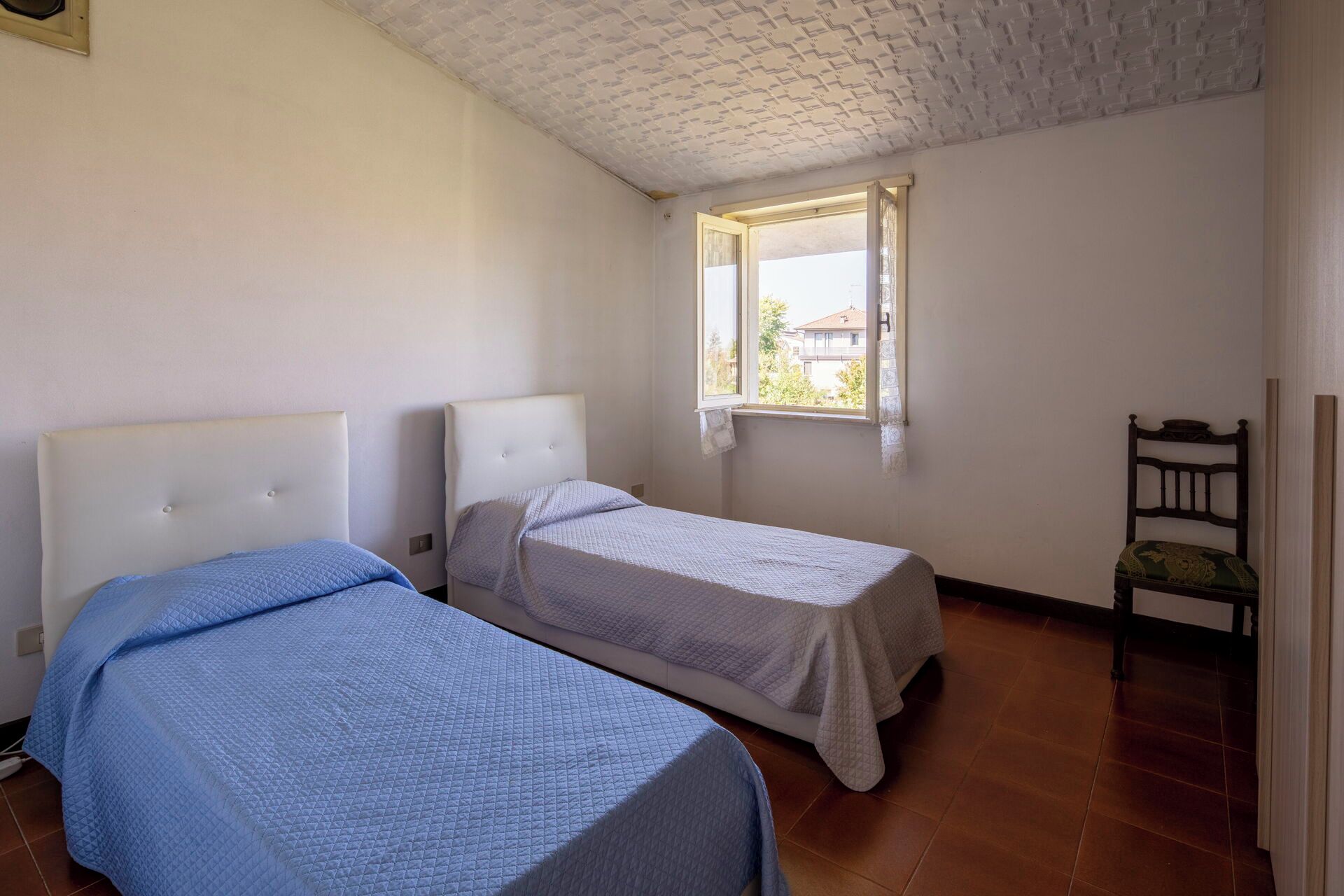 A room with two beds, a window, and a chair.