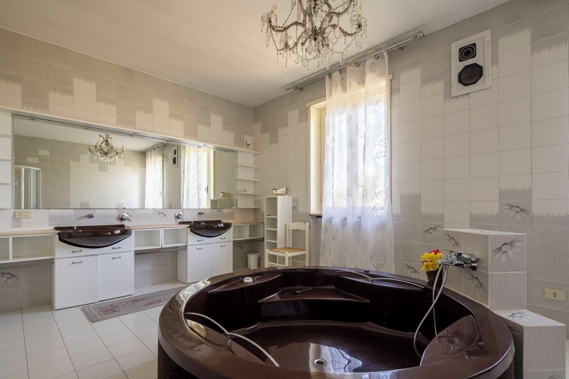 A bathroom with a large bathtub, a double vanity with mirrors, and a chandelier.