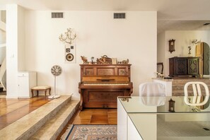 A living room with a wooden piano, a white chair, a glass table, and a patterned rug.