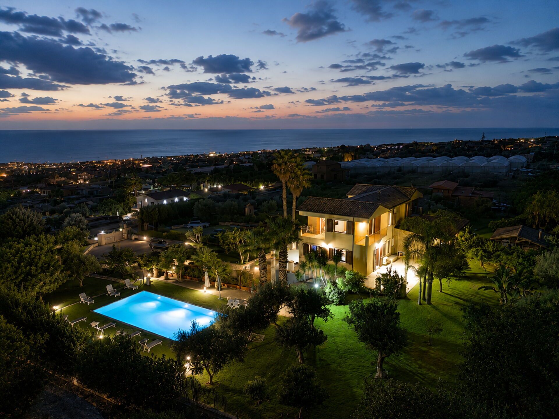 Une propriété résidentielle dotée d’une piscine, d’une végétation luxuriante et offrant une vue sur la mer au crépuscule.