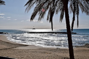 Ein Strand mit Palmen, ein Boot in der Ferne und eine Felsformation.