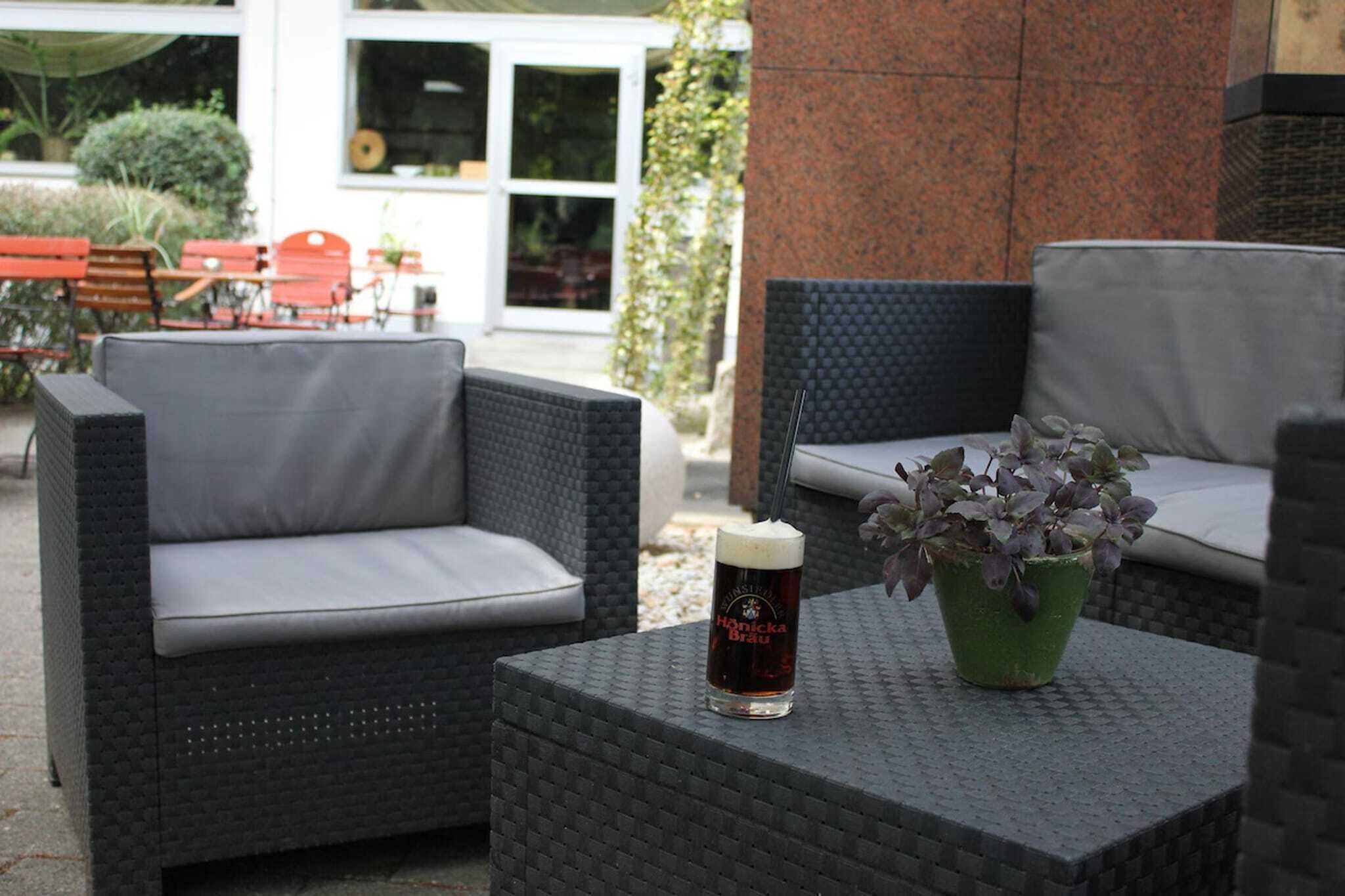 Mobiliario de mimbre exterior con cojines, una cerveza en un vaso y una planta en maceta.