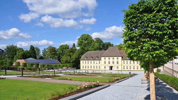 A large building with a symmetrical facade, surrounded by a well-maintained lawn and a paved walkway.