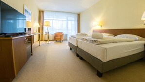 A hotel room with a TV, a desk, two beds, a chair, and a window with curtains.