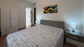 Een slaapkamer met een bed, een kledingkast, een nachtkastje, een lamp en een schilderij aan de muur.