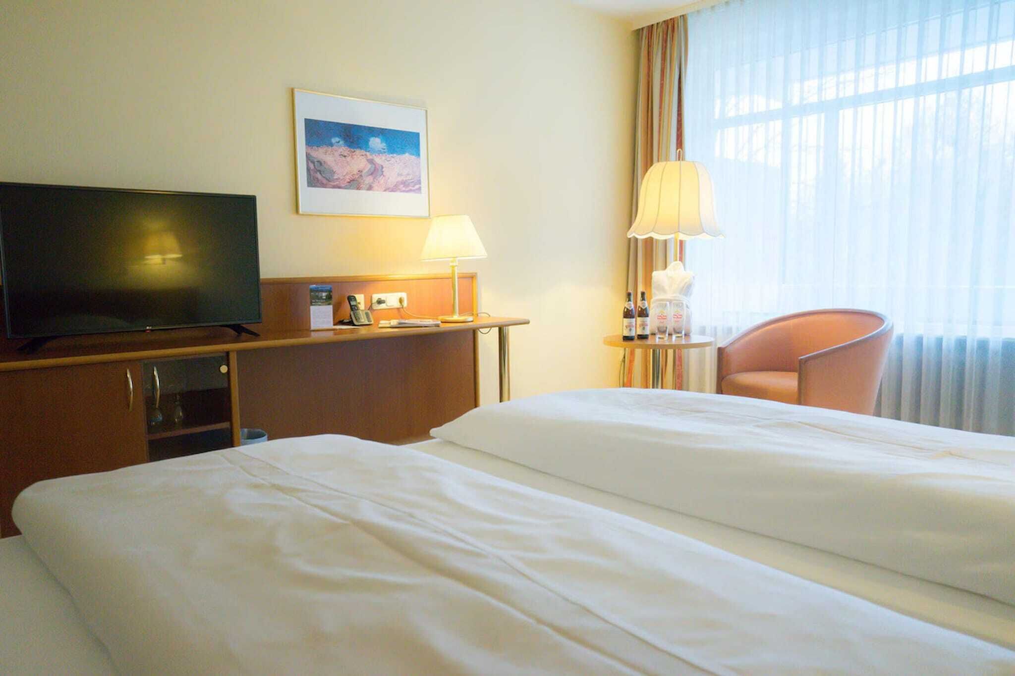 Een hotelkamer met een bed, een televisie, een bureau met lamp, een stoel en een raam met gordijnen.
