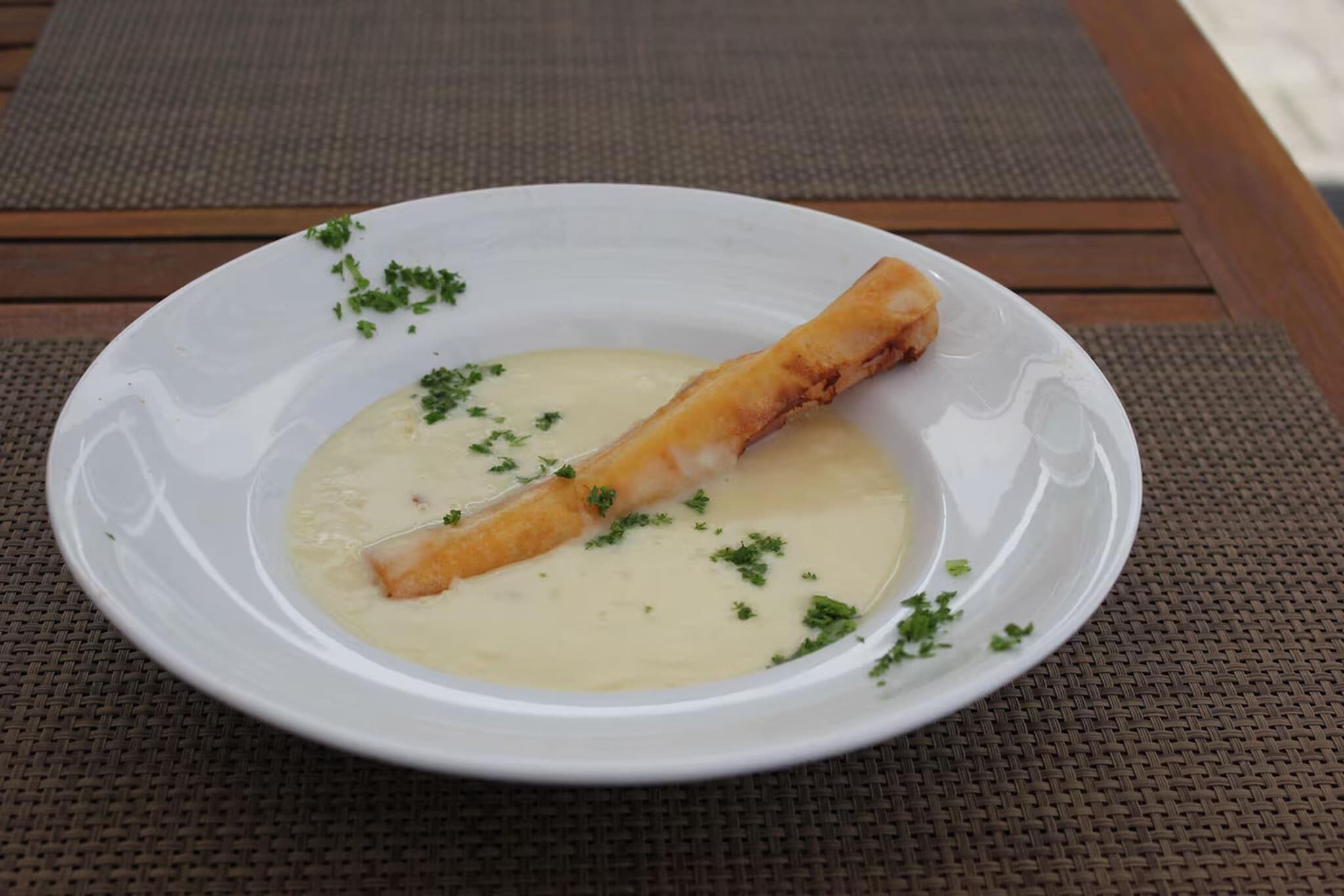 Een witte schaal met een opgerolde portie en een romige saus, versierd met groene kruiden, op een geweven placemat.