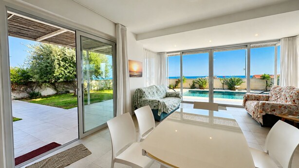 Ein modernes Wohnzimmer mit Glastür, die auf eine Terrasse, einen Pool und Meerblick führt.