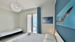 Ein Hotelzimmer mit einem großen Bett, einem kleineren Bett, einer Hängeleuchte, einem Fenster mit Vorhängen und einem Wandbild mit Vogelmotiv.
