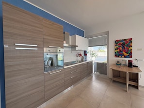 A modern kitchen with wooden cabinets, a built-in oven, and a window overlooking a balcony. - Villa in Marina Di Ragusa with 3 bedrooms sleeps 7 (Marina Di Ragusa)