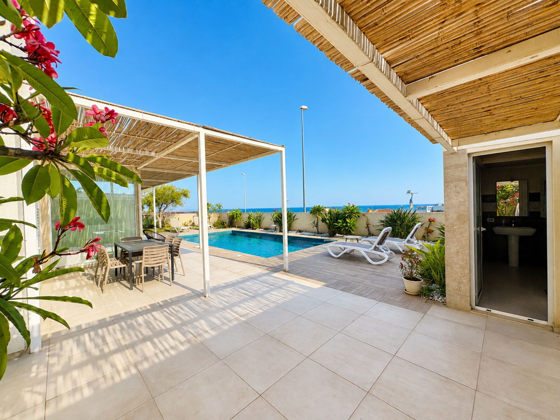 A covered outdoor area with a pool, lounge chairs, and a dining table.