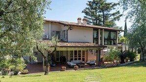 A two-story house with a covered patio, a lawn, and a stone pathway. - Villa El Perlè by Geco Vacation Rentals (Padenghe Sul Garda)