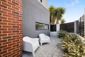 A modern outdoor patio with two white chairs, a brick wall, and a metal fence.