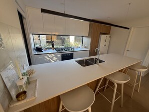 A modern kitchen with a central island, bar stools, and a view of the outdoors.