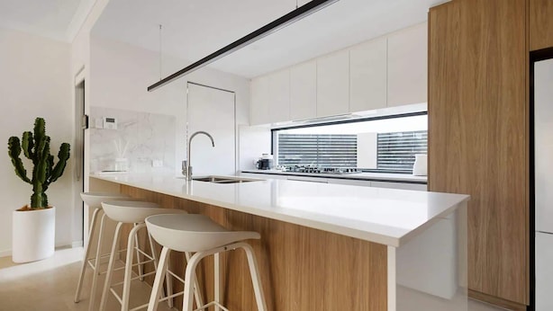 A modern kitchen with a white countertop, stainless steel sink, and wooden accents.