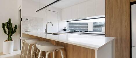 A modern kitchen with a white countertop, stainless steel sink, and wooden accents.