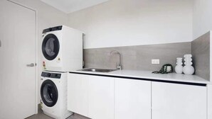 A compact kitchen with a washing machine, a sink, and white cabinets.