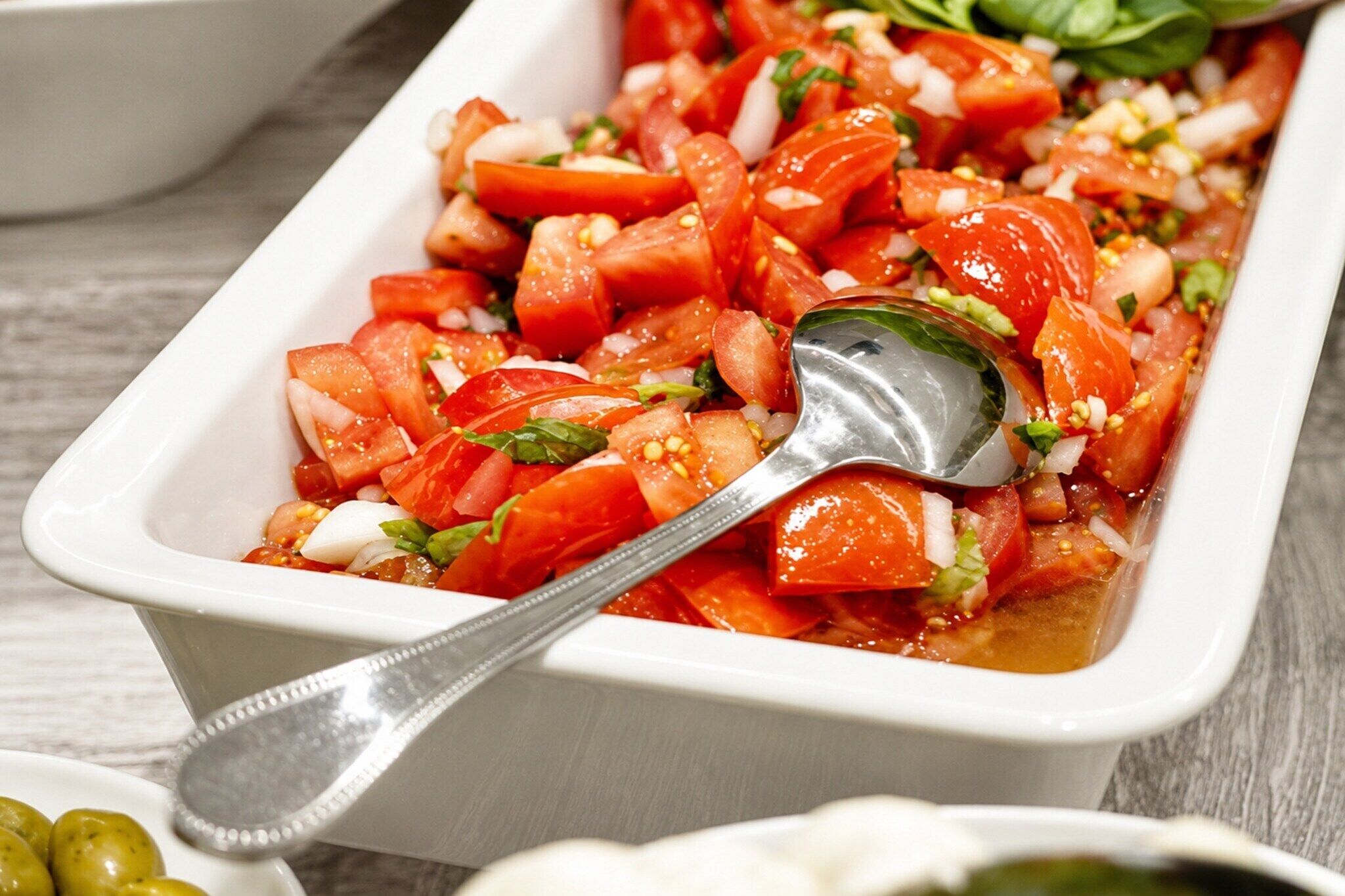 Un plat rectangulaire blanc contenant des tomates coupées en dés, des herbes aromatiques et une cuillère.