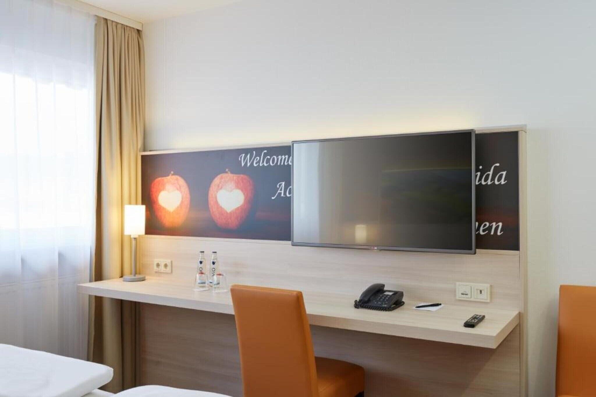 Een hotelkamer met een bureau, twee stoelen, een televisie, een telefoon en een lamp.