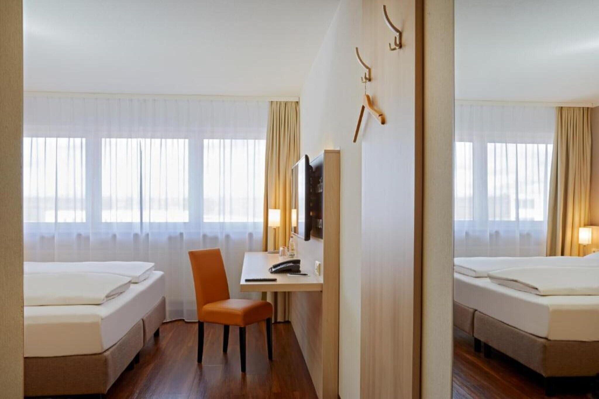 Ein Hotelzimmer mit zwei Betten, einem Schreibtisch, einem Stuhl, einem Fernseher und einem Fenster mit Vorhängen.