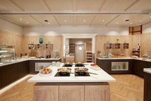 Une cuisine moderne avec des meubles en bois, un îlot central doté de différents espaces de cuisson et une vue sur la salle à manger.