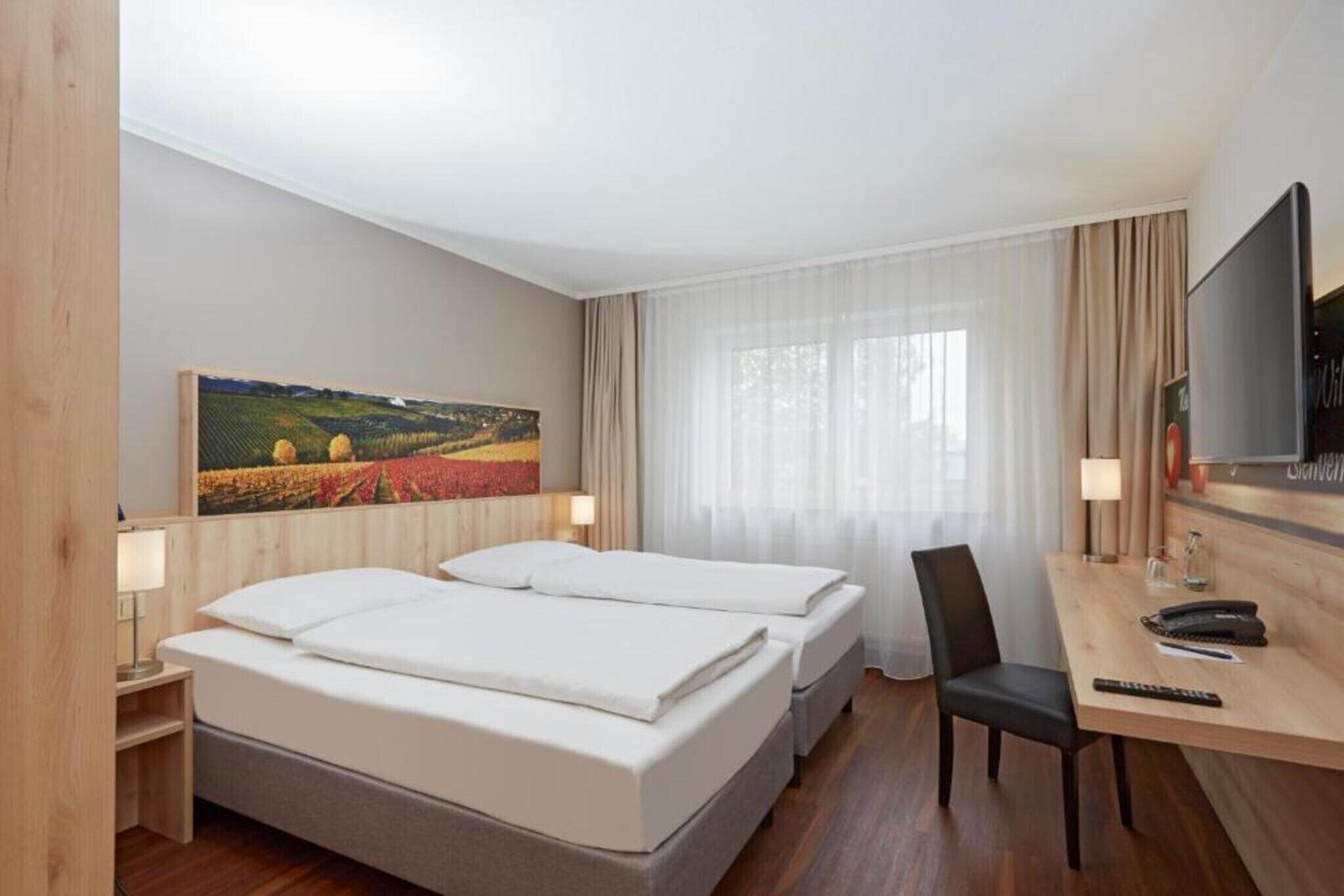 A hotel room with two beds, a desk, a chair, a TV, and a painting on the wall.