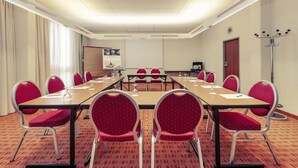A conference room with a long table, red chairs, a projector screen, and a coat rack. - Sunday Hotel Berlin City West Standard Single Room (Berlin)