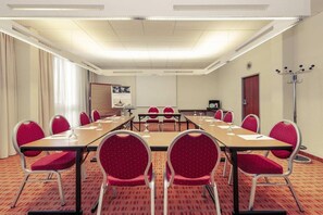 Ein Konferenzraum mit einem langen Tisch, roten Stühlen, einer Projektionsleinwand und einem Garderobenhaken.