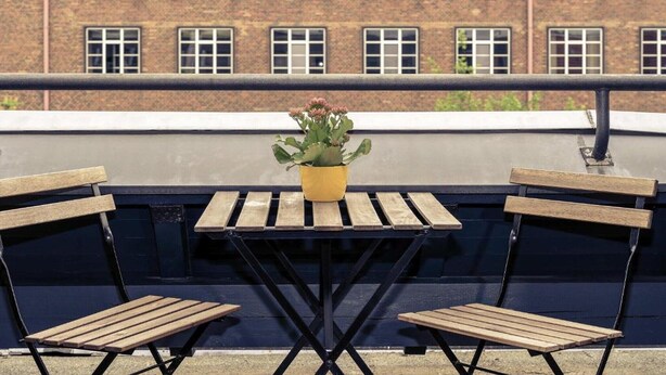 A rooftop terrace with a table and two wooden chairs, a potted plant, and a brick building in the background. - Sunday Hotel Berlin City West Standard Single Room (Berlin)