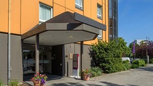 A hotel entrance with a covered area, glass doors, and potted plants. - Sunday Hotel Berlin City West Standard Single Room (Berlin)