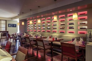 Ein Restaurant mit mehreren Tischen und Stühlen, einer Wand mit beleuchteten Nischen und Decken mit Einbauten.