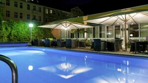 A swimming pool with lounge chairs and umbrellas, surrounded by a building with large windows. - Sunday Hotel Berlin City West Standard Single Room (Berlin)