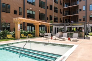 Un área de piscina de hotel con una zona de estar cubierta, sillas de descanso y una estación de barbacoa.